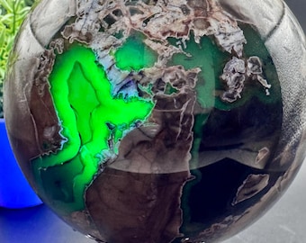 May include: A polished green and black agate sphere on a silver stand. The sphere has a swirling pattern of green and black.