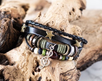 May include: A multi-layered leather bracelet with a braided black leather strap, silver and gold metal beads, and a silver musical note charm. The bracelet also features small gold star charms.