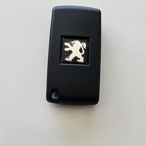 May include: Black car key with a silver Peugeot logo.