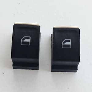 May include: Two black plastic car window switches with silver trim. Each switch has a white icon of a car door.