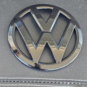 Peut inclure: Un emblème Volkswagen noir brillant de forme circulaire avec un design stylisé en "V".