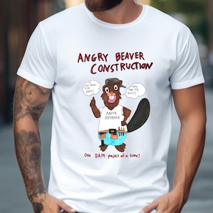 Puede incluir: Camiseta blanca con un castor de dibujos animados y el texto "ANGRY BEAVER CONSTRUCTION". El castor lleva un sombrero, un cinturón de herramientas y pantalones cortos azules. Los bocadillos dicen "I can never find SH!T!" y "Who took my lunch!" También se incluye la frase "One DAM project at a time!"