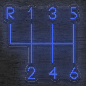 Op de afbeelding: Een blauw neon-bord met een 6-versnellings handgeschakelde transmissie-schakelpatroon. De nummers 1, 2, 3, 4, 5 en 6 worden op het bord weergegeven, samen met de letter "R" voor de achteruitversnelling.