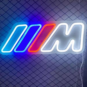 May include: Neon sign featuring the BMW M logo. The sign has a white outline with the iconic M colors: light blue, dark blue, and red. The sign is illuminated with neon lights, creating a vibrant and eye-catching display.
