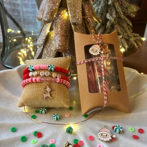 May include: A set of Christmas-themed charm bracelets with red, white, and green beads. The bracelets are packaged in a brown box with a red and white ribbon. The box also contains a small Santa charm.