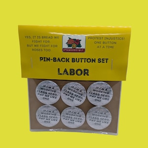 May include: A set of six circular pin-back buttons on a brown backing card with a yellow header. Each button features a wood grain texture and the black text: IF I'M A WORKING CLASS HERO, PAY ME LIKE ONE. The header includes the text: YES, IT IS BREAD WE FIGHT FOR, BUT WE FIGHT FOR ROSES TOO. PROTEST INJUSTICE! ONE BUTTON AT A TIME.