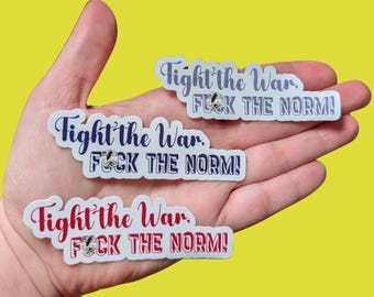 May include: A hand holding several stickers with the text "Fight the War, FUCK THE NORM!" in various colors. The stickers have a white border and are on a yellow background.