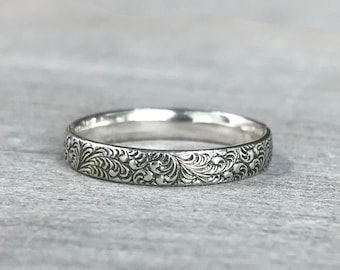 Puede incluir: Un anillo de banda de plata con un intrincado diseño floral.