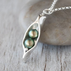 May include: A silver necklace with a pea pod pendant featuring two green pearls.