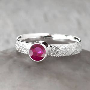 May include: A silver ring with an intricate floral design and a bright pink gemstone.
