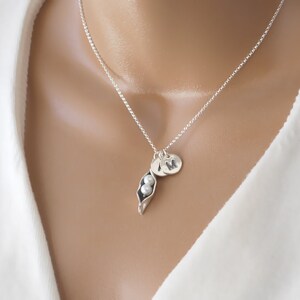 May include: A silver necklace with a pea pod charm and two pearl beads. The necklace also has a silver initial charm with the letter "M" on it.