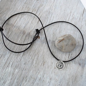 May include: A black leather cord necklace with a silver anchor pendant. The pendant is round and features a raised anchor design.