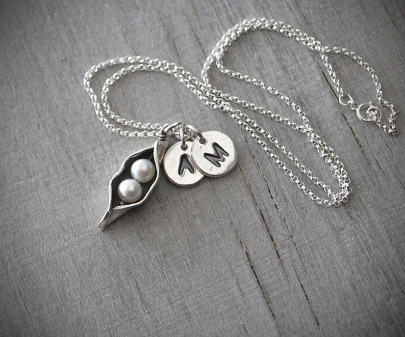 May include: A silver necklace with a pea pod charm containing two pearls and two initial charms, 'A' and 'M'.