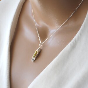 May include: A silver chain necklace with a pea pod charm. The charm is made of silver and has three gold peas inside.