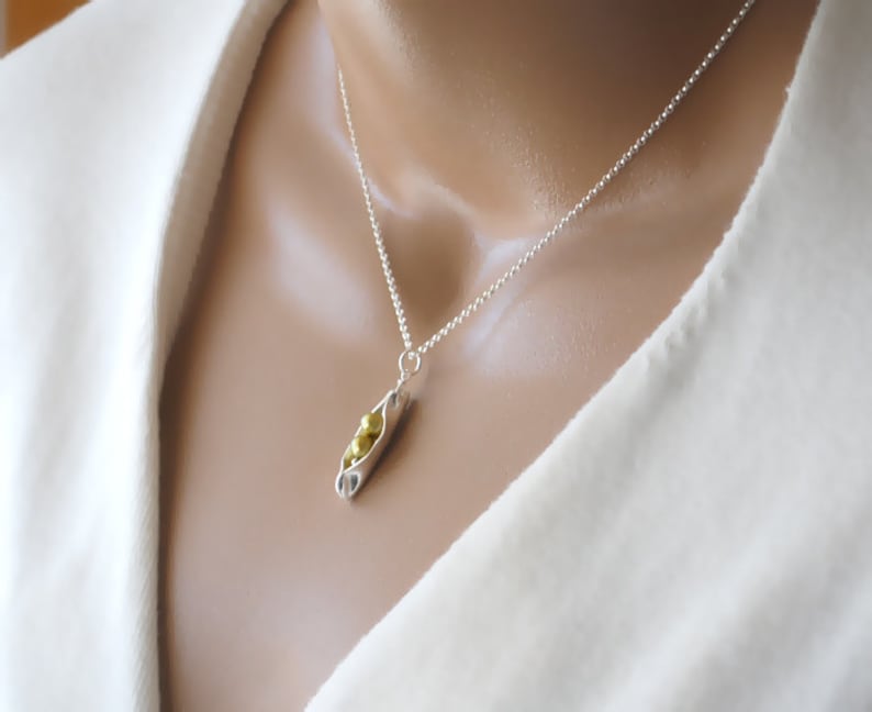 May include: A silver chain necklace with a pea pod charm. The charm is made of silver and has three gold peas inside.