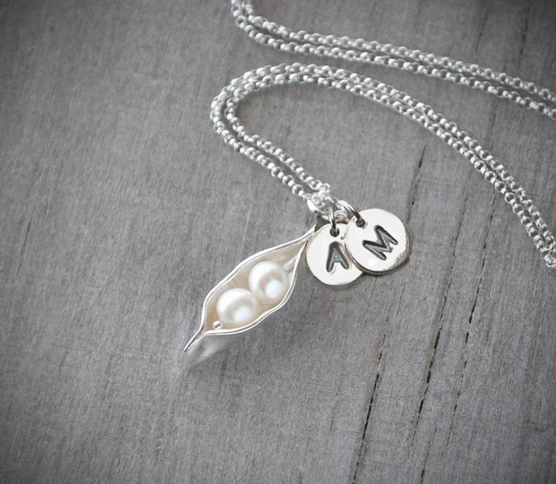 May include: A silver necklace with a pea pod charm containing two white pearls and two silver initial charms with the letters 'A' and 'M'.