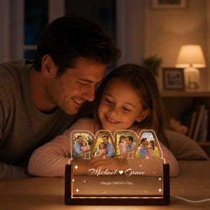 May include: A personalized Father's Day gift featuring a wooden base with a glowing acrylic panel. The panel spells "DADA" and displays family photos. The base has the names "Michael & Grace" and the text "Happy Father's Day".