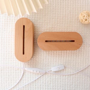 May include: Two wooden LED light bases with a white cord and switch. One base is vertical with a long slot, the other is horizontal with a row of lights. The bases are oval-shaped and made of light-colored wood.