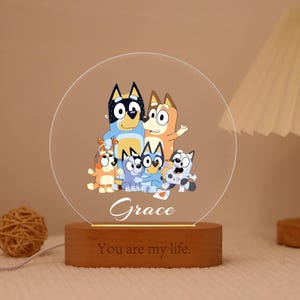 May include: A decorative night light featuring a cartoon family of dogs. The clear, circular acrylic panel displays the family with the name "Grace" below. The wooden base has the text "You are my life." The light emits a warm glow.