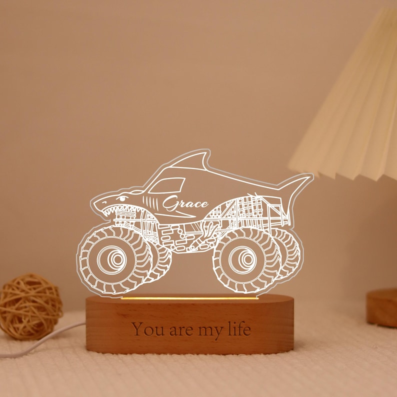 May include: A shark-themed monster truck night light with the name "Grace" etched on the side. The light sits on a wooden base with the words "You are my life" engraved. The truck has large, detailed wheels.