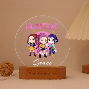 Può includere: Luce notturna personalizzata con un'immagine a cartoni animati di tre ragazze e il testo rosa "HUNTRAX". La base in legno ha il nome "Grace" e la frase "You are my life" incisi.