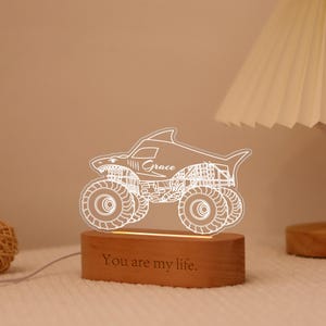 May include: A shark-shaped monster truck night light with the name "Grace" etched on the side. The light sits on a wooden base with the phrase "You are my life" engraved. The light is white and the base is brown.
