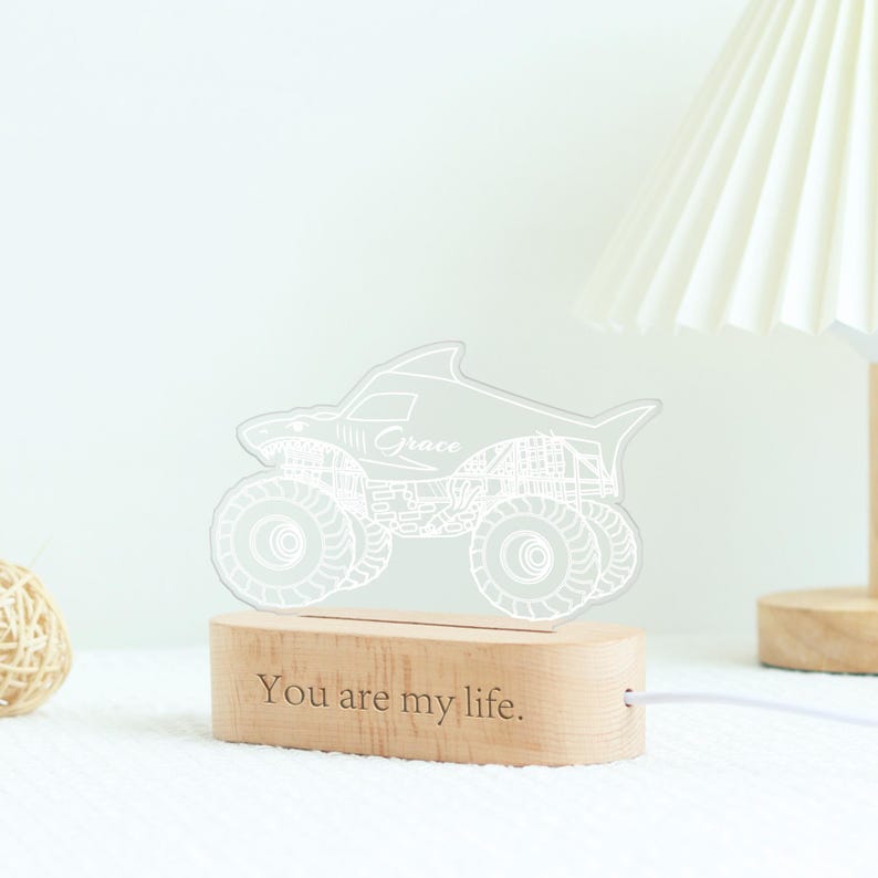 May include: A shark-shaped monster truck night light with the name "Grace" etched on the side. The light sits on a wooden base with the text "You are my life." The light is connected to a white cord.