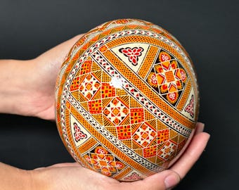 May include: A hand-painted Easter egg with a geometric pattern in shades of orange, red, black, and white.