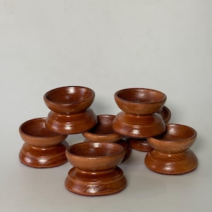 May include: A collection of small, handcrafted wooden bowls. Each bowl is a rich, warm brown color with a smooth, glossy finish. The bowls are stacked in small groups, showcasing their unique shape and design. These decorative bowls are ideal for serving small portions.