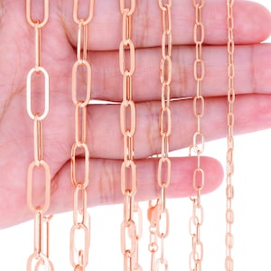 May include: Several rose gold chain necklaces of varying styles are displayed against a hand. The chains feature different link designs, including elongated oval and smaller, more delicate links. The chains are all a warm, metallic color.