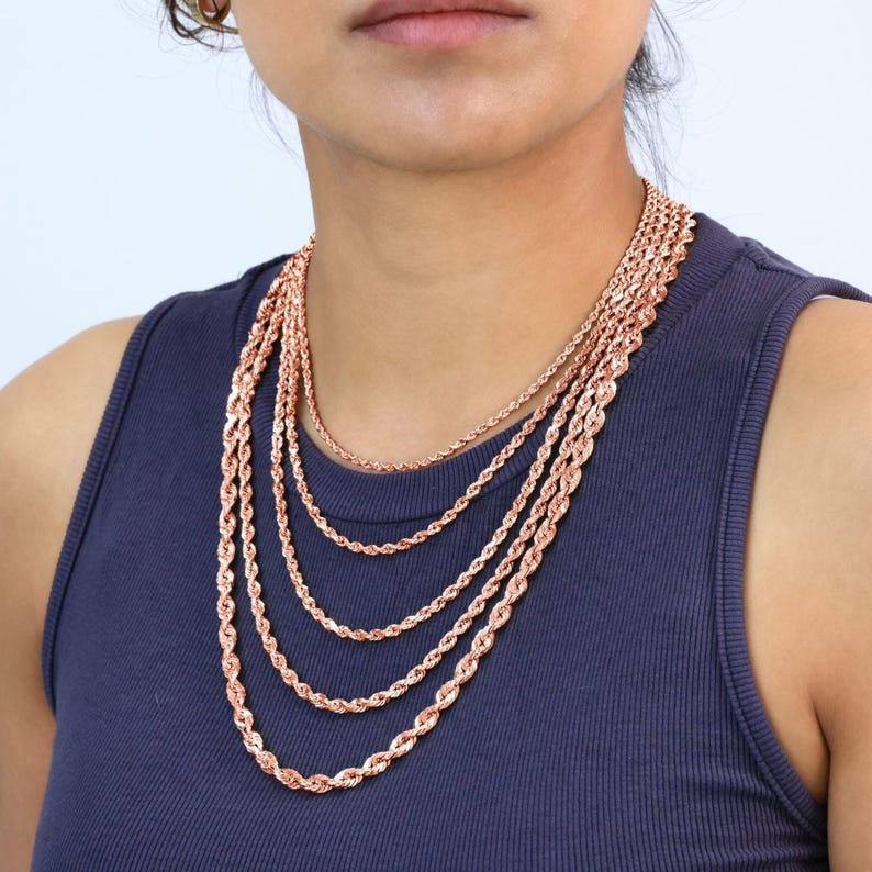 Puede incluir: Un conjunto de cinco cadenas de cuerda de oro rosa de diferentes longitudes. Las cadenas est&aacute;n superpuestas y las lleva una persona.