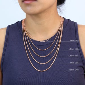 Puede incluir: Cinco cadenas de cuerda de oro rosa de diferentes tama&ntilde;os, que van desde 1 mm hasta 2,5 mm de grosor. Las cadenas se muestran en una modelo que lleva un top azul sin mangas. Las cadenas est&aacute;n etiquetadas con su grosor y longitud en pulgadas. 1 mm - 16 pulgadas, 1,5 mm - 18 pulgadas, 1,8 mm - 20 pulgadas, 2 mm - 22 pulgadas, 2,5 mm - 24 pulgadas.