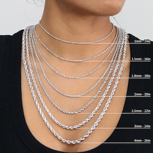 May include: A close-up of a model wearing a variety of silver rope chains of different lengths and thicknesses. The chains are labelled with their thickness and length in inches. 1mm - 14in, 1.5mm - 16in, 1.8mm - 18in, 2mm - 20in, 2.5mm - 22in, 3mm - 24in, 4mm - 26in.