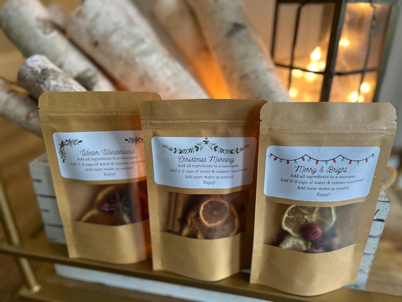 Op de afbeelding: Drie bruine papieren zakjes met verschillende kerstthema-etiketten en ingredi&euml;nten erin. De etiketten luiden "Winter Wonderland", "Christmas Morning" en "Merry & Bright".