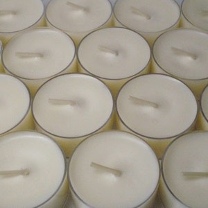 May include: A close-up view of a large quantity of white tea light candles arranged in rows. The candles are all the same size and shape, and they have a small wick in the center.