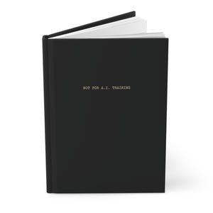 Puede incluir: Un diario de tapa dura negro con el texto "NOT FOR A.I. TRAINING" en letras doradas. El diario está abierto, revelando páginas blancas. La cubierta es de color negro liso y el lomo es visible.