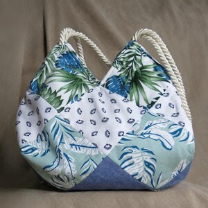Peut inclure: Sac à dos patchwork avec un motif de feuilles tropicales en bleu, vert et blanc. Le sac a une base en jean et des poignées en corde crème. Le sac mesure environ 30 cm de haut et présente un motif géométrique unique.