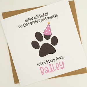 May include: A white birthday card with a brown envelope. The card features a black paw print wearing a pink party hat and the text "happy birthday to the bestest dog auntie". The card also says "Lots of Love from Bailey".