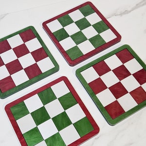 Puede incluir: Cuatro posavasos cuadrados con un patrón de tablero de ajedrez. Dos posavasos tienen un patrón de tablero de ajedrez rojo y blanco con un borde verde. Dos posavasos tienen un patrón de tablero de ajedrez verde y blanco con un borde rojo.