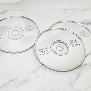Puede incluir: Tres discos compactos en blanco plateados con el texto "Sonic CD-R Disc 700MB" impreso en cada uno.