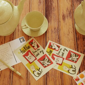 May include: Two postcards with a yellow background and red and black cat illustrations. The postcards say "hello from me and my cat". A handwritten postcard with a message to Mom and Dad. A teapot, teacup, and saucer in a light yellow color. A small stack of vintage stamps with floral designs.
