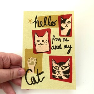 May include: A yellow card with red and gold accents features three cartoon cats. The text on the card reads "hello from me and my cat".