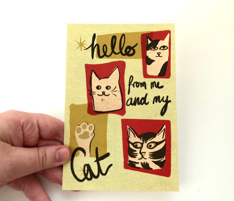 May include: A yellow card with red and gold accents features three cartoon cats. The text on the card reads "hello from me and my cat".