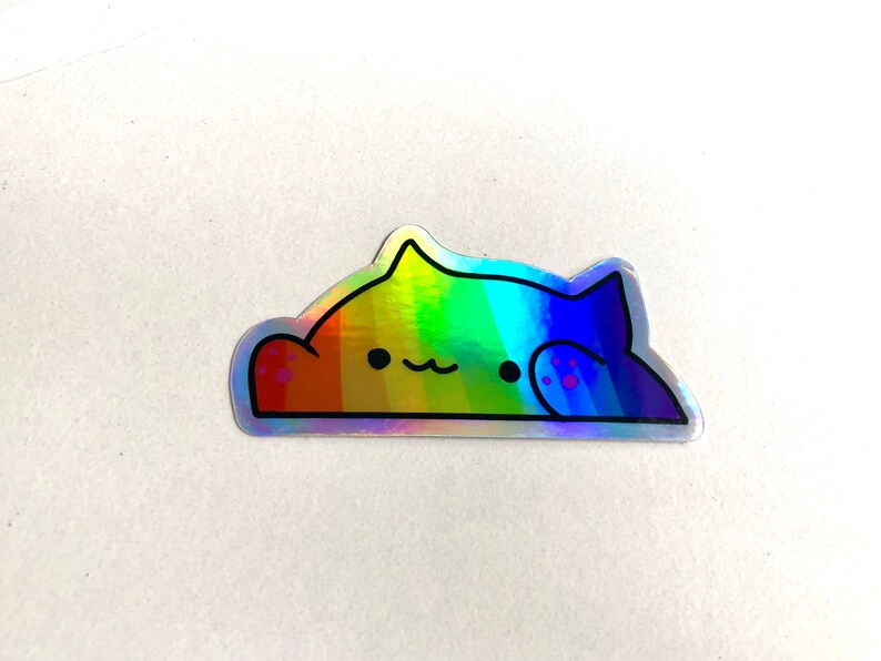 May include: A rainbow holographic sticker of a cat with a paw print on its back. The cat is laying down with its head resting on its paw.