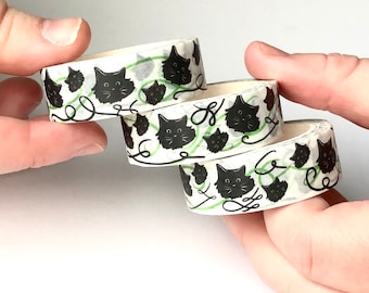 May include: Three rolls of washi tape with a black cat design on a white background. The cats are surrounded by green vines and swirls.
