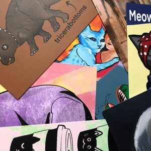 Puede incluir: Una colecci&oacute;n de tarjetas coloridas con varias ilustraciones. Una tarjeta presenta un triceratops de dibujos animados con el texto "triceratops" y flechas que apuntan a su cabeza y cola. Otra tarjeta presenta un gato de dibujos animados con un pa&ntilde;uelo rojo con lunares blancos y el texto "Meow Can Do".