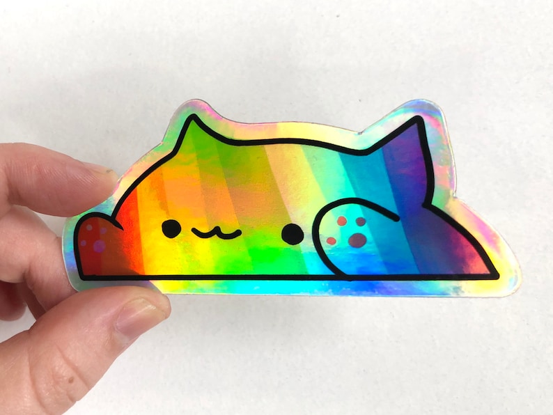 May include: A rainbow iridescent vinyl sticker of a cartoon cat with a paw print on its back. The cat is lying down with its eyes closed and a small smile on its face.