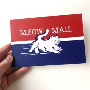 Op de afbeelding: Een rood, wit en blauwe kaart met de tekst "MEOW MAIL" en een witte kat die met zijn staart in de lucht rent.
