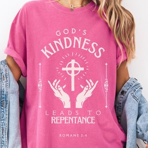 May include: Pink t-shirt with a white graphic design that says "God's Kindness Leads to Repentance" with a cross and hands reaching up. The text "Romans 2:4" is also included on the shirt.
