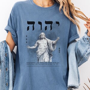 May include: A blue t-shirt with a graphic of a man with outstretched arms and the Hebrew word "יהוה" above him. The text below the graphic reads "God replied 'I AM WHO I AM. This is what you are to say, I AM has sent me to you.' Ex. 3:14"